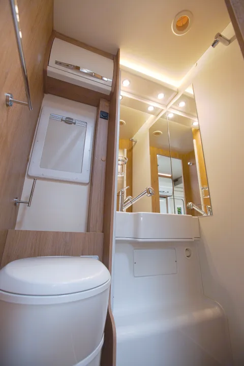 Compact RV rental bathroom: toilet, sink with faucet, large mirror, and shower base, all illuminated by recessed lights.. rollerteam 747 2021