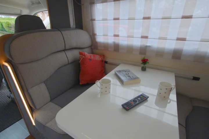 Cozy RV rental dinette featuring comfortable seating, a table with a book, mugs, and remote, plus ambient lighting.. rollerteam 747 2021