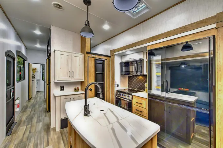 Spacious, modern RV rental kitchen with an island, stainless steel appliances, and light wood tones for comfortable travel.. Heartland RVs Milestone 2023