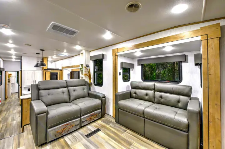 Modern RV rental living room with two comfortable gray sofas, wood trim, recessed lighting, and scenic window views.. Heartland RVs Milestone 2023