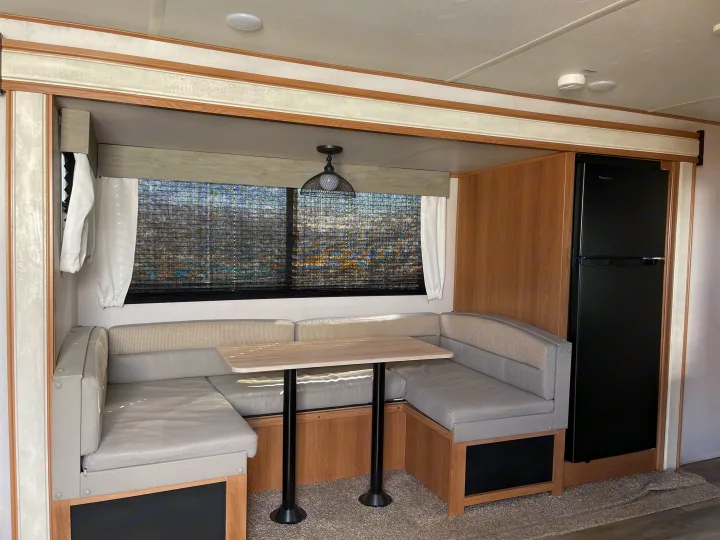 RV rental interior: bright dinette with U-shaped seating, table, window, and a large black refrigerator for comfortable travel.. Avenger Avenger Trailer 2022