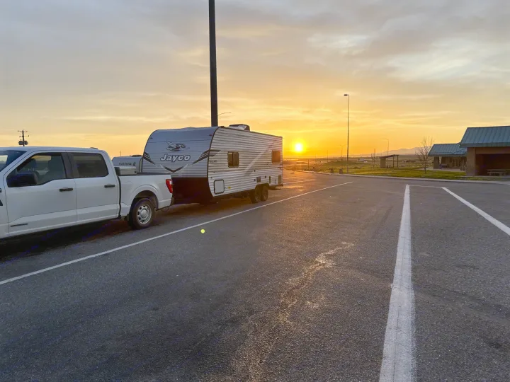 White truck with a Jayco RV rental in a parking lot, illuminated by a stunning sunset. Perfect for road trip adventures.. Jayco Jay Flight SLX 2025