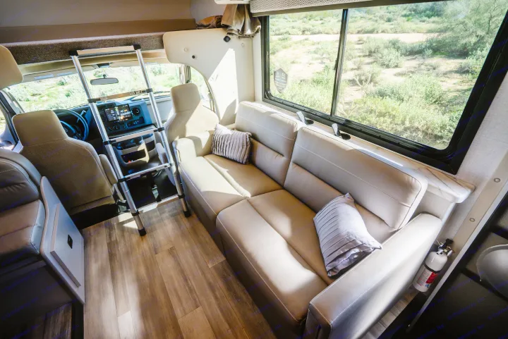 Spacious RV rental interior featuring a cozy sofa, cockpit, and a window view of the desert. Ladder to bunk above.. Thor Geneva 2026