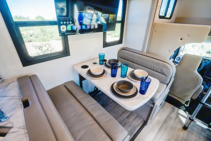 Enjoy an RV rental with a dining nook, smart TV (webOS Hub menu visible), set table, and scenic views from large windows.. Thor Geneva 2026