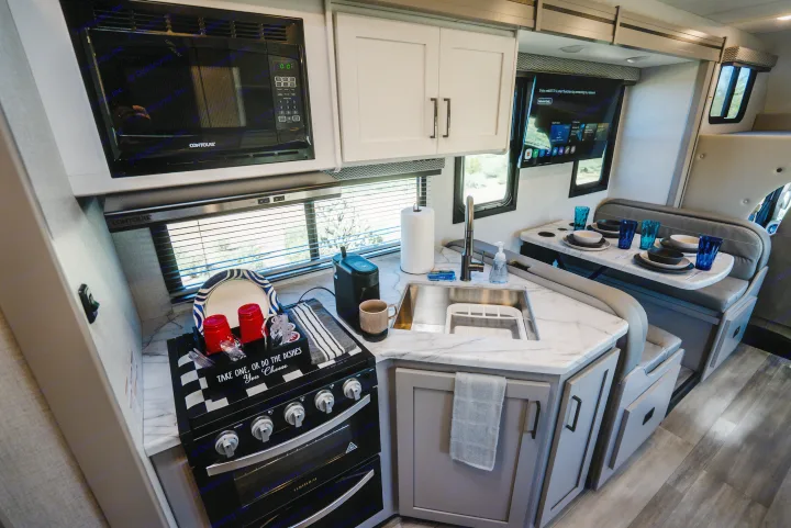 Modern RV rental kitchen & dining area: microwave, stove, sink, coffee maker, and comfortable booth seating with TV.. Thor Geneva 2026