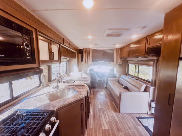Bright rv rental interior: kitchen with microwave, sink, stovetop, dining booth, sofa lounge, and driver's cabin.. Thor Four Winds 2022