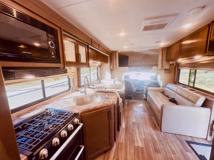 Spacious RV rental interior featuring a full kitchen with microwave, stove, sink, dining area, and comfy sofa for your travels.. Thor Four Winds 2022