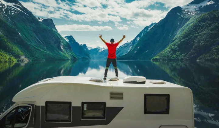 Elevate your journey with an rv rental! Man on camper roof celebrates stunning fjord and mountain reflections on tranquil water.. Thor Four Winds 2022