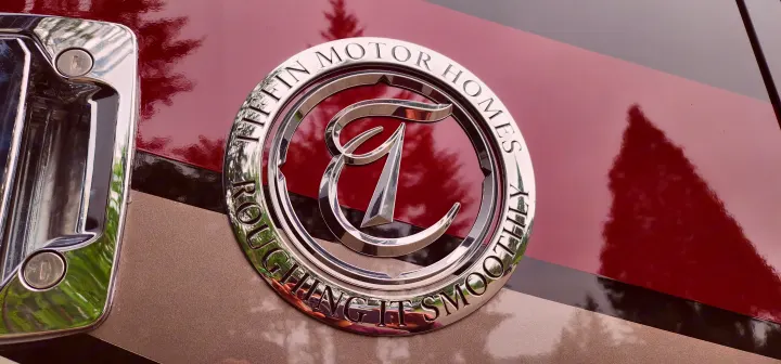 Close-up of a Tiffin Motor Homes luxury RV rental emblem, featuring "Roughing It Smoothly" text on its chrome design.. Allegro Allegro Open Road 2023