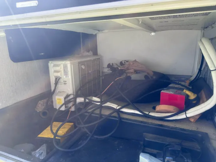 This RV rental's utility bay features a mounted mini-split AC unit, various hoses, electrical cables, and stored gear.. Coachmen Crosstrek 23XG 2021