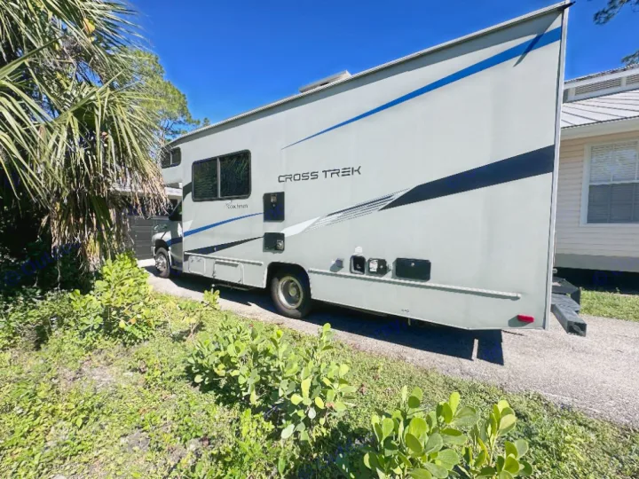 Spacious grey RV for rent, a Coachmen Cross Trek motorhome, parked on a driveway with palm trees nearby.. Coachmen Crosstrek 23XG 2021