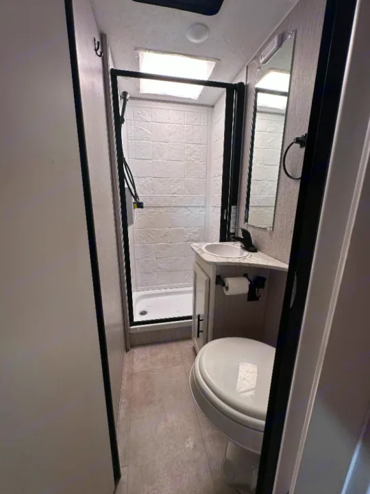 Compact RV rental bathroom: shower with a skylight, toilet, sink, and mirror. Clean and functional for travelers.. Coachmen Crosstrek 23XG 2021
