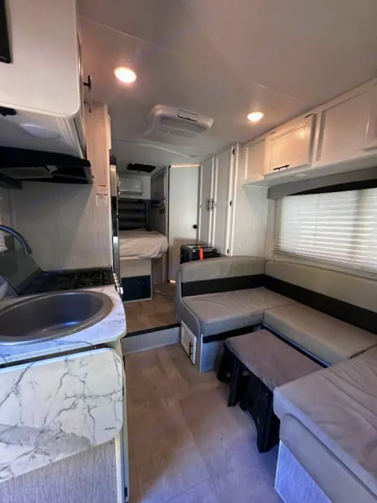 L-shaped dinette, kitchen, and bed inside a modern RV rental, offering comfortable and compact living for travel.. Coachmen Crosstrek 23XG 2021