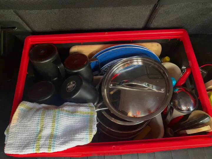 Organized camping kitchen gear in a red crate, perfect for an RV rental adventure. Includes pots, pans, dishes, mugs, and utensils.. Subaru Outback 2015