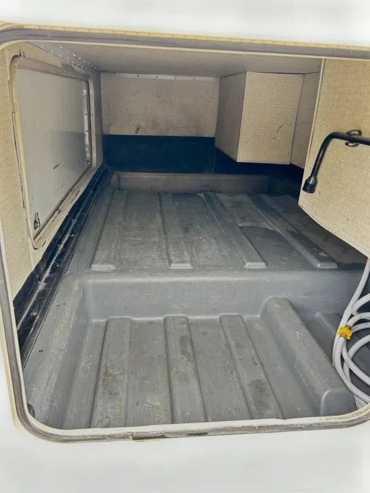 Empty RV rental exterior storage compartment, featuring a molded floor, side panel, and coiled hose on the right.. Winnebago Minnie Winnie 2018