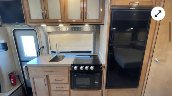 Explore this RV rental's modern kitchen: sink, stovetop, microwave, and fridge with a bed reflection. Perfect for trips!. Thor Quantum 2021