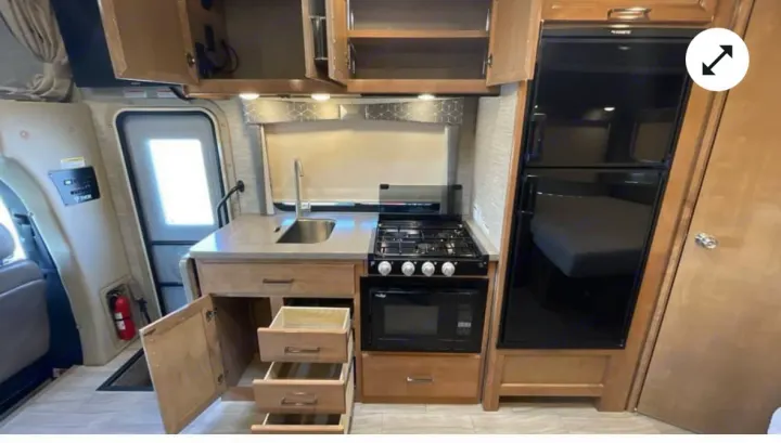 Explore this RV rental's compact kitchen, featuring a sink, stovetop, microwave, fridge, and light wood cabinets for your travels.. Thor Quantum 2021