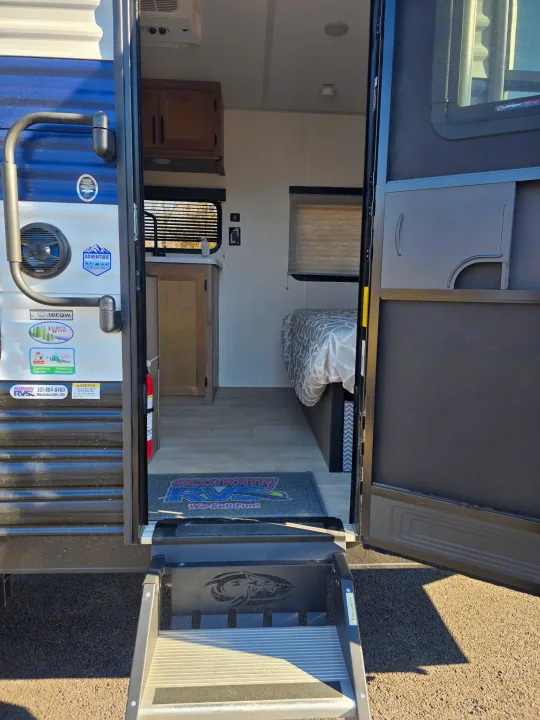 Inside a spacious travel trailer RV rental, featuring an inviting entrance, compact kitchen, and comfortable bed for your journey.. Forest River Cherokee Wolf Pup 2025