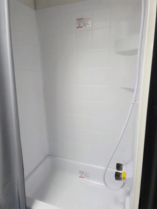Clean, compact RV rental shower stall with white textured walls, flexible shower head, controls, and a shower curtain.. Forest River Cherokee Wolf Pup 2025