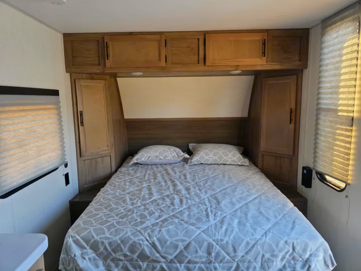 RV rental's cozy bedroom. This compact space includes a patterned bed, wood cabinets, and window blinds.. Forest River Cherokee Wolf Pup 2025