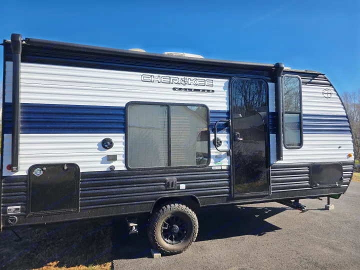 This Cherokee Wolf Pup travel trailer, a stylish black and white RV rental, is parked on asphalt under a clear blue sky.. Forest River Cherokee Wolf Pup 2025