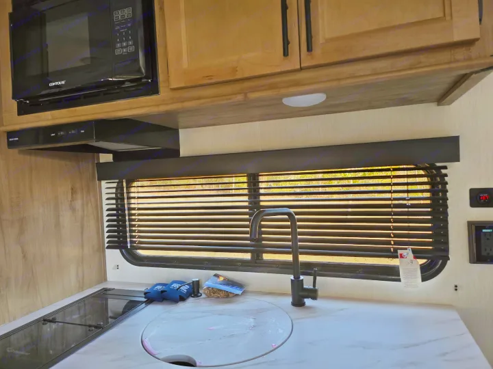 RV rental kitchen showing a modern sink, faucet, stovetop, microwave, and range hood with window blinds.. Forest River Cherokee Wolf Pup 2025