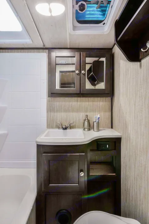 This RV rental bathroom features a dark wood vanity, white sink, overhead mirrored cabinet, and shower. Toiletries are on the counter.. Cruiser RV Shadow Cruiser 2019
