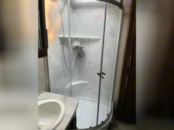 Clean RV rental bathroom featuring a corner shower, sink, and storage. Ideal for comfortable travels on your adventure.. Keystone RV Cougar 2021