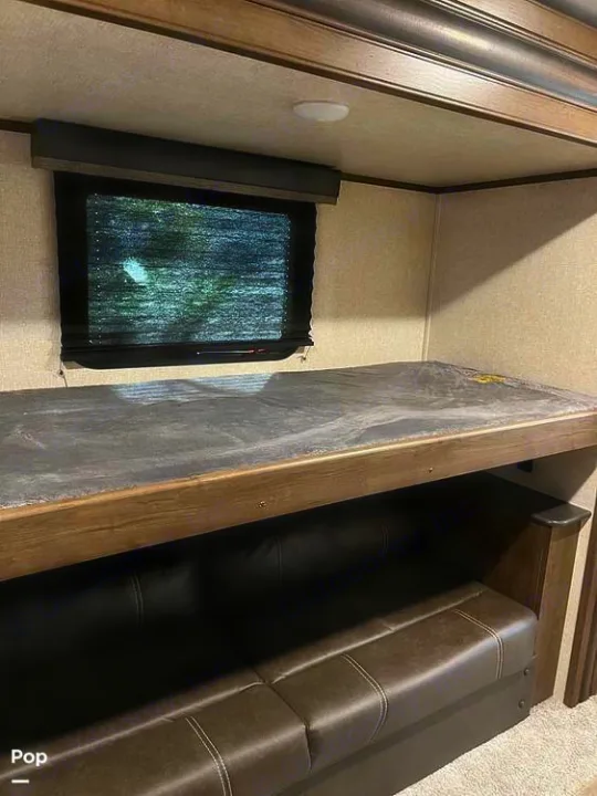 Cozy RV rental interior: Bunk bed above a brown sofa, with a window and shades in a compact living space.. Keystone RV Cougar 2021
