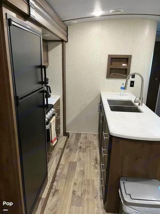 Modern RV rental galley kitchen interior featuring a large black fridge, sink, stove, and wood-look flooring.. Keystone RV Cougar 2021