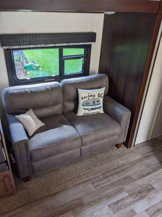 Cozy two-seater sofa in an RV rental, with a window revealing green outdoors and a pillow urging 'enjoy the journey'.. Jayco Jay Feather 2019