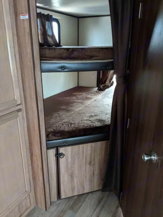 Inside an RV rental: view of cozy bunk beds with dark privacy curtains and a window. Ideal sleeping area for a family camper.. Jayco Jay Feather 2019