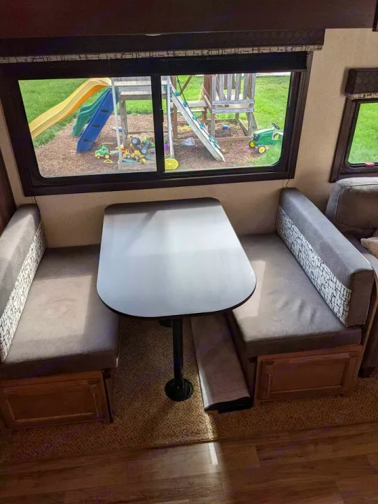 Inside an RV rental: a dinette with bench seating and table, offering a view of a backyard playground through the window.. Jayco Jay Feather 2019