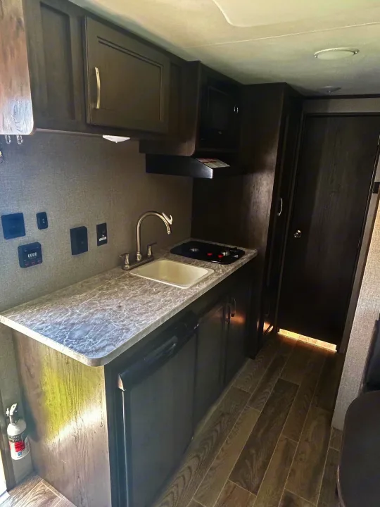 Compact RV rental kitchen featuring a sink, stove, microwave, fridge, cabinets, and fire extinguisher. Ready for travel.. Jayco Jay Flight SLX 2021