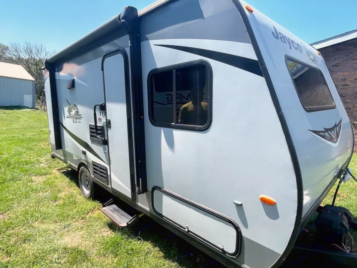 Gray Jayco travel trailer RV rental on grass, featuring an awning & steps. Perfect for your outdoor adventures!. Jayco Jay Flight SLX 2021