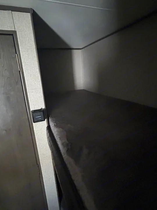 This dark RV rental bunk bed area features a control panel next to a door, offering a compact sleeping space.. Jayco Jay Flight SLX 2021