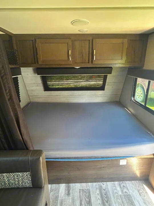 RV rental bedroom showcasing a spacious bed, overhead wood cabinets, windows with blinds, and sleek flooring.. Jayco Jay Flight SLX 2021