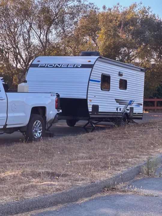 White pickup truck with a Pioneer travel trailer, set up as an rv rental at a sunny outdoor spot.. Heartland RVs Pioneer 2025