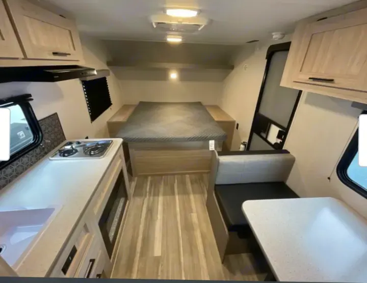RV rental interior featuring a modern kitchen with stove, sink, microwave, a bed, and dinette seating with a table.. Heartland RVs Pioneer 2025