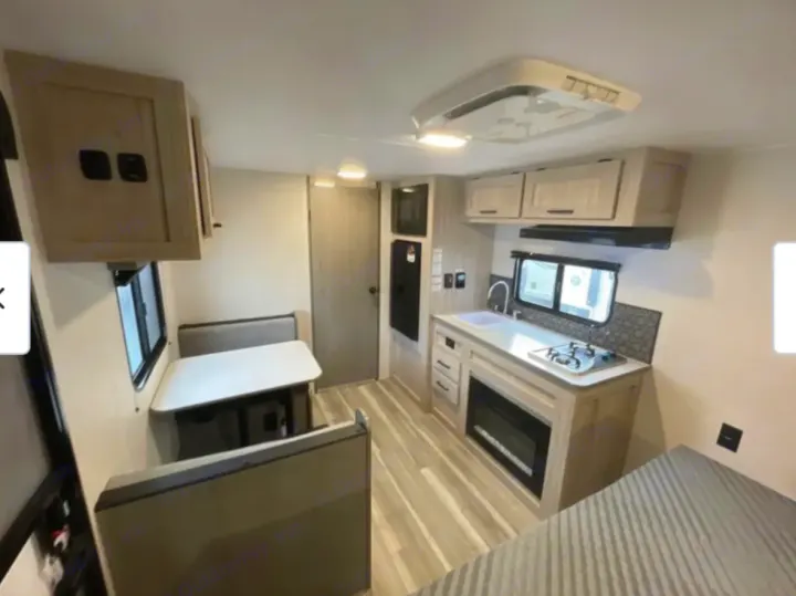 Light-toned rv rental interior: modern kitchenette with stove, sink, dinette with bench seating. Ready for your travels.. Heartland RVs Pioneer 2025