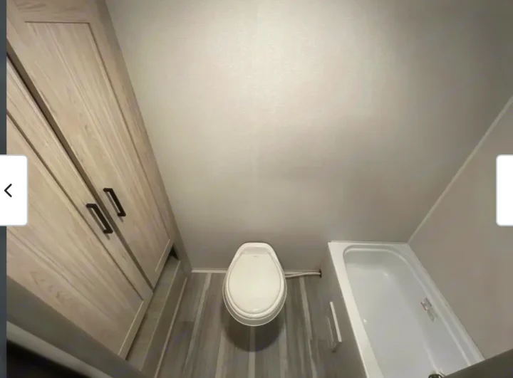 This RV rental bathroom features a white toilet, compact bathtub, and tall wood-grain cabinet on grey wood-look flooring.. Heartland RVs Pioneer 2025