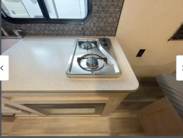 This RV rental kitchen boasts a 2-burner stove, sleek countertop, and microwave below, with a sink to the left.. Heartland RVs Pioneer 2025