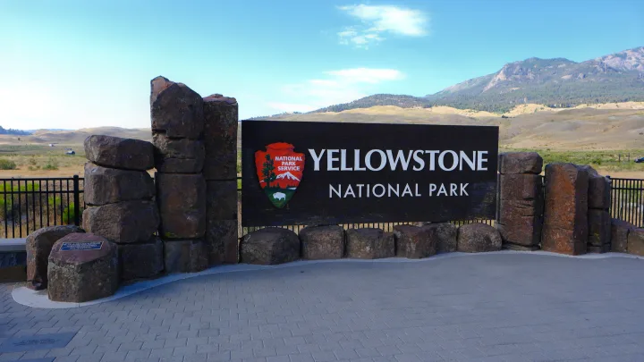 Yellowstone National Park's iconic entrance sign, made of large stones, set against scenic mountains. Ideal for an RV rental road trip.. Ford Roofnest 2024