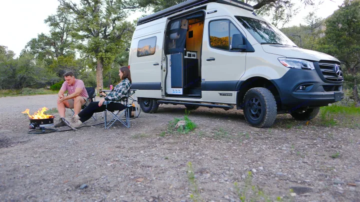 Relaxing by a campfire with an RV rental. A couple enjoys the outdoors next to their Winnebago camper van.. Mercedes Winnebago 2024