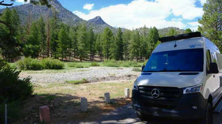 A Mercedes-Benz Sprinter RV rental parked in a scenic mountain forest with tall pine trees and a dry rocky riverbed.. Mercedes Winnebago 2024