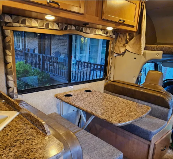 RV rental interior: dinette seating, kitchen, and large window offering a view of a home porch. Comfortable travel space.. Thor Chateau 2016