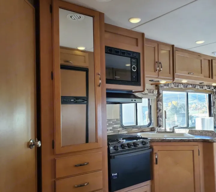 This RV rental kitchen features a black stove/oven, microwave, sink, and wood cabinets. A mirrored door conceals the fridge.. Thor Chateau 2016