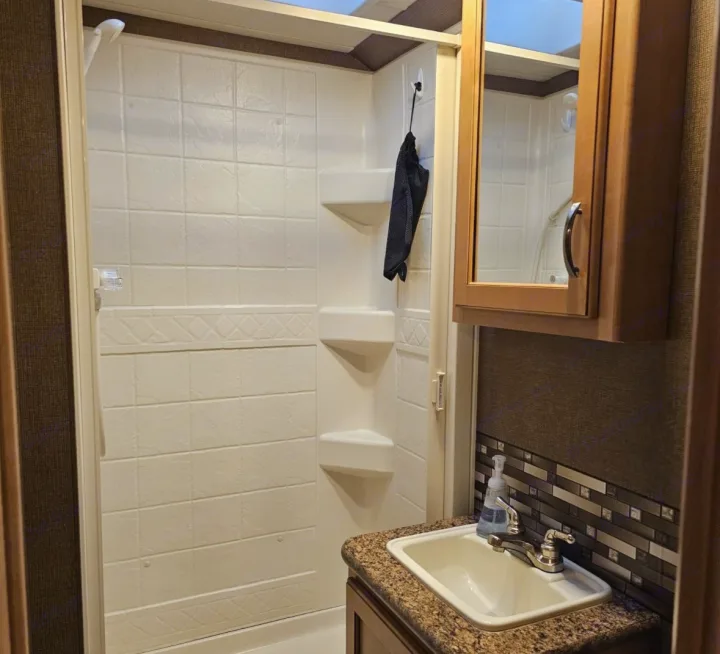 RV rental bathroom, featuring a white shower with built-in shelves and a vanity with a sink and mosaic backsplash.. Thor Chateau 2016