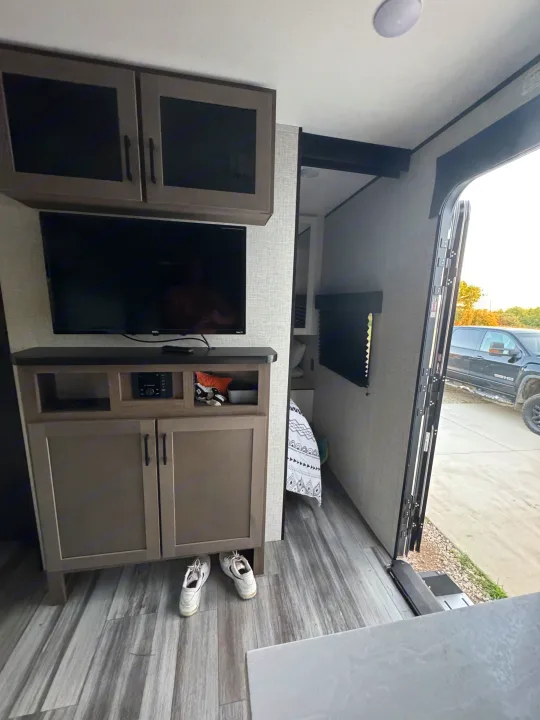 Cozy RV rental interior with TV, media console, storage, and bedroom access. The open door reveals a truck parked outside.. Jayco Jay Flight SLX 2025