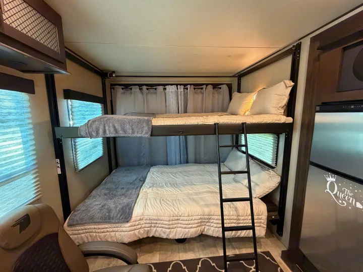 View inside an RV rental showing stacked bunk beds, complete with white bedding, gray blankets, and a ladder.. Grand Design Momentum Toy Hauler 2022